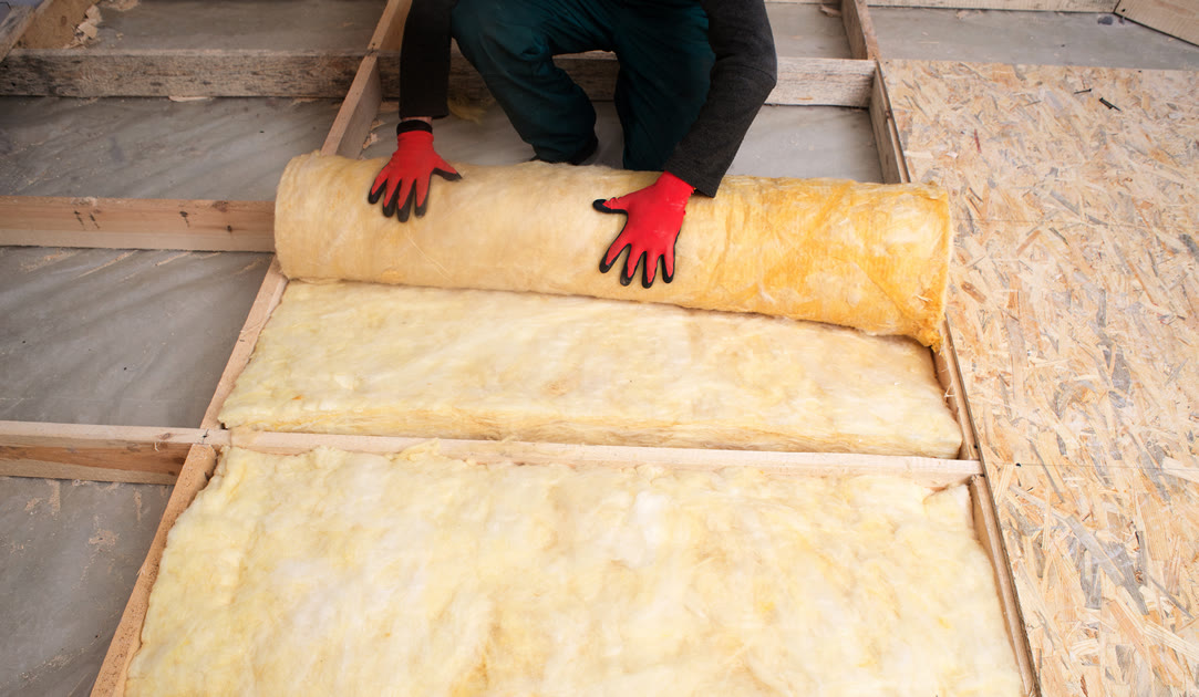Pose de rouleaux isolants entre les solives d'un plancher en bois.