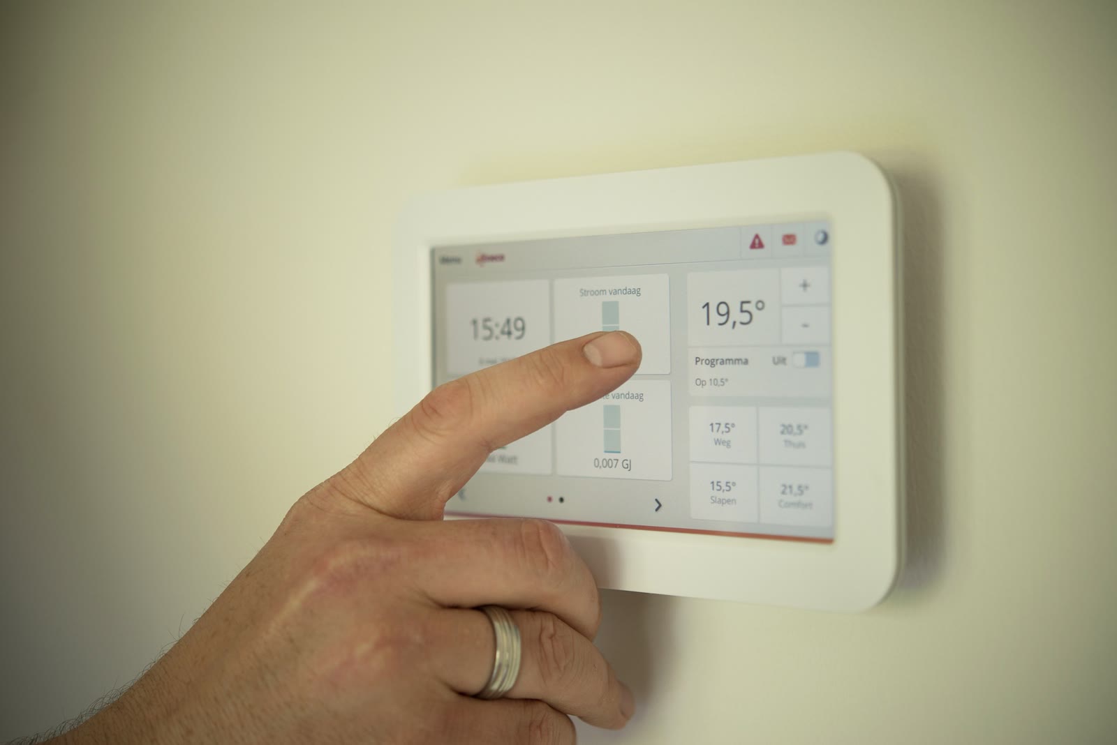 Main réglant un thermostat mural.